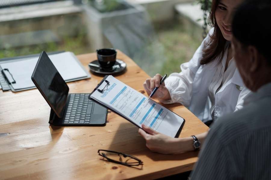 A female advisor guiding a client through an insurance claim form on a clipboard during a professional meeting.