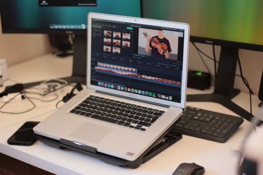 An open laptop on a desk showing video editing software with a timeline and video previews.