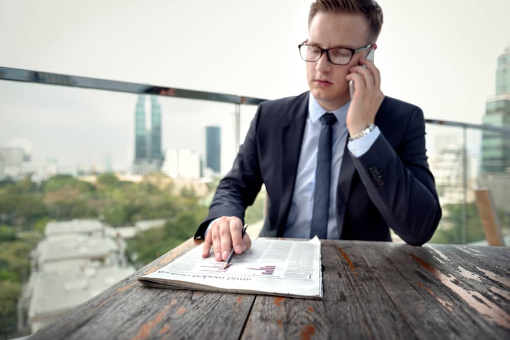 Un homme en costume analyse des graphiques financiers tout en passant un appel téléphonique. L'image illustre le concept de navigating the legalities and tax regulations.