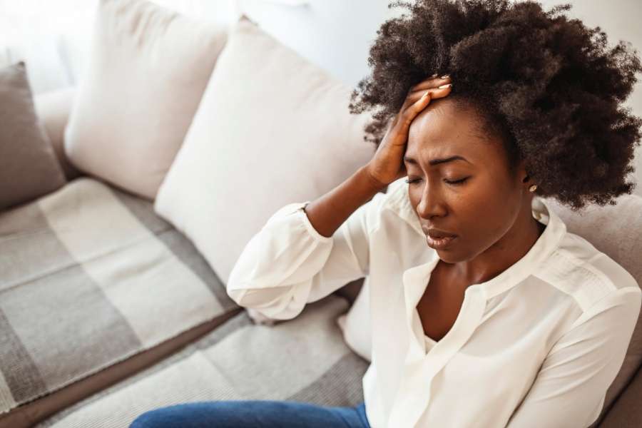 A stressed Black woman holding her head while sitting on a couch, feeling completely burned out.