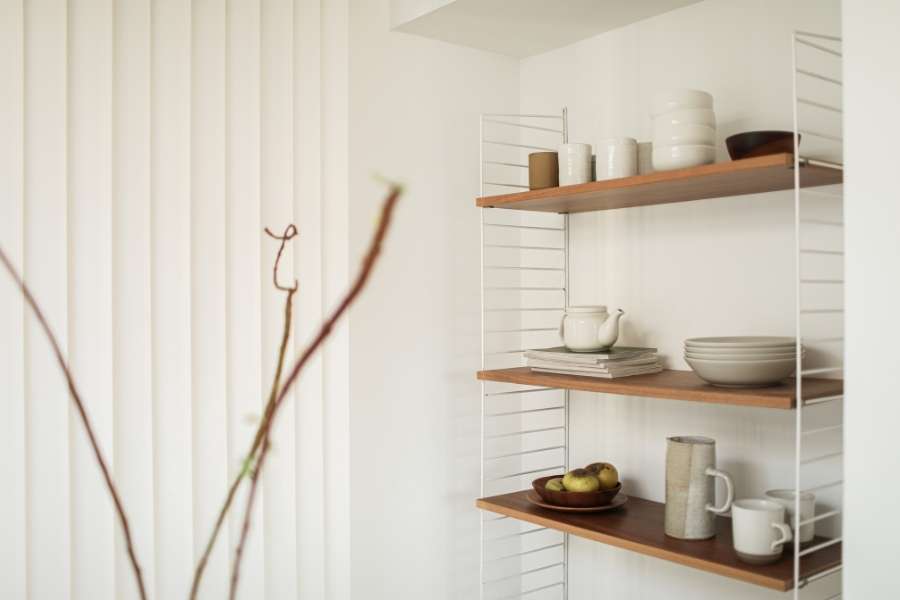 Wooden shelves with white wire frame supports mounted against a white wall and holding ceramic kitchenware.