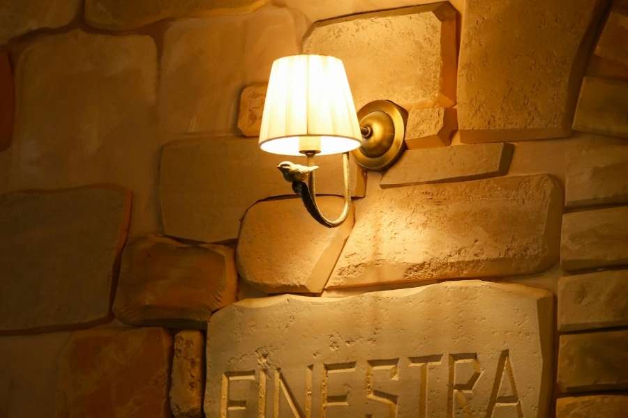 A rustic wall light layering warm ambient illumination over a textured stone wall with carved lettering.